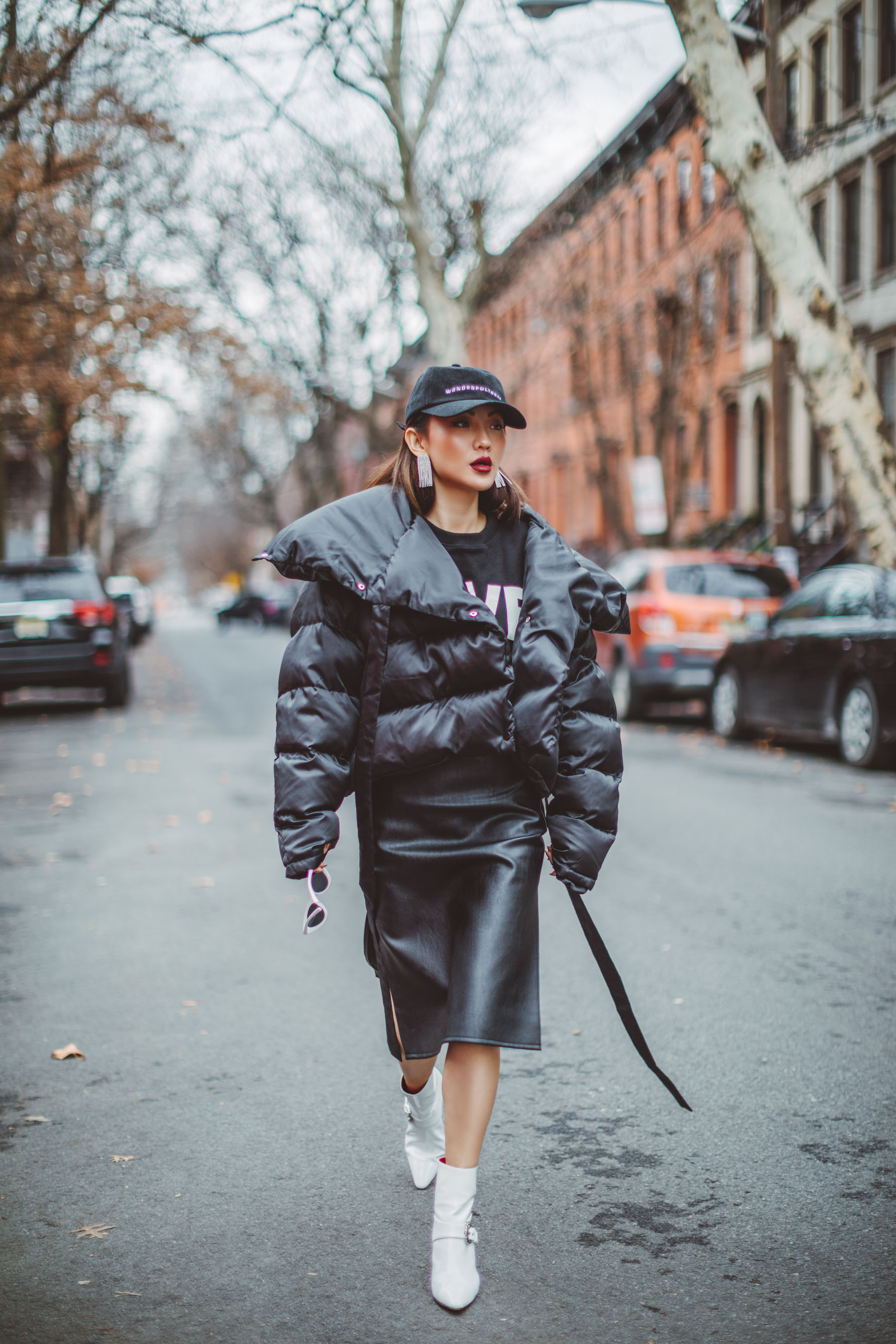 How to Look Stylish in a Quilted Puffer Jacket // Notjessfashion.com // Black quilted puffer jacket, white ankle boots, black oversized sweater, leather skirt, urban outfit, edgy fashion look, baseball cap, pink sunglasses, new york fashion blogger, asian blogger, how to dress edgy, new york street style, edgy street style